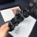 Front view of black satin headband showing hand-finished ruffle and soft bubble accent