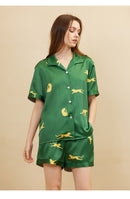 Woman wearing dark green silk pajama set in bedroom setting