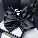 Front view of large black satin bow hair clip on white background