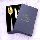 Overhead flat lay of gold fork, knife, and spoon aligned symmetrically on marble surface
