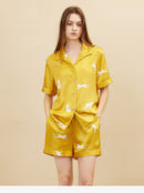 Lifestyle shot of woman wearing gold silk pajama set lounging on sofa