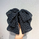 Front view of black polka dot bow hair clip on neutral background