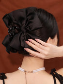 Black satin bow hair clip worn with a silk scarf and minimalist earrings